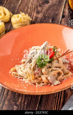 Pasta Fettuccine mit Pilzen und gebratenem Hühnerschinken in cremiger Form Käsesauce auf hellem Holzhintergrund Stockfoto