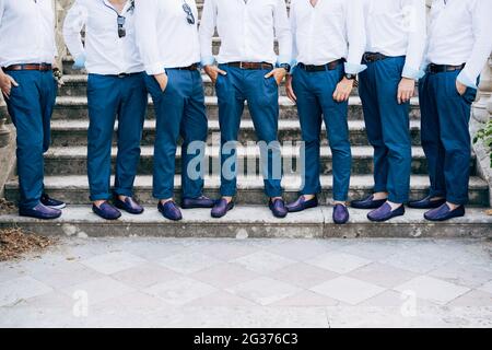 Die besten Männer des sieben Bräutigams in identischen blauen Hosen und Schuhen stehen aus nächster Nähe auf der Treppe Stockfoto