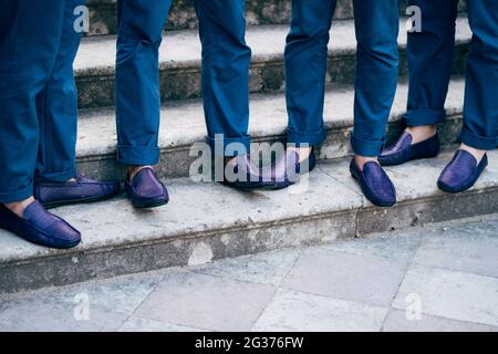 Die besten Männer des sieben Bräutigams in identischen blauen Hosen und Schuhen stehen aus nächster Nähe auf der Treppe Stockfoto