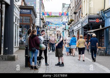 Geschäftige Straßenszene in Falmouth, die Menschen unterschiedlichen Alters während des G7-Klimaereignisses vor dem Hintergrund von Geschäften unter Straßenbannern zeigt. Stockfoto