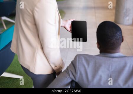 Mittlerer Abschnitt der Geschäftsfrau, die im Büro einem behinderten Geschäftsmann im Rollstuhl ein digitales Tablet zeigt Stockfoto