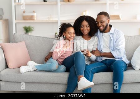 Glückliche afroamerikanische Familie hält und mit Smartphone zu Hause Stockfoto