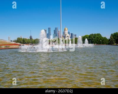 Jets von Springbrunnen an einem sonnigen Tag vor der Kulisse moderner Wolkenkratzer und einem wolkenlosen blauen Himmel. Erholungsgebiet im Victory Park auf Poklonnaya Stockfoto