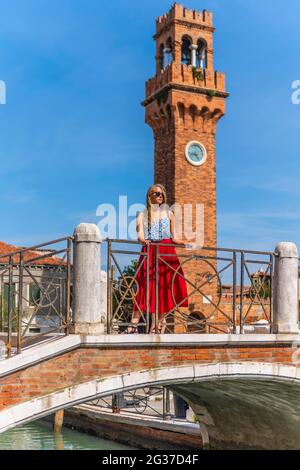 Junge Frau an einem Kanal, Häuser und Boote am Kanal Rio del Vetrai, Glockenturm St. Stefano, Murano, Venedig, Venetien, Italien Stockfoto