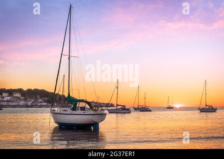 Instow, North Devon, England. Die Flut geht zurück, wenn die Sonne hinter den Segelbooten untergeht, die am Strand im malerischen Küstendorf I festgemacht sind Stockfoto