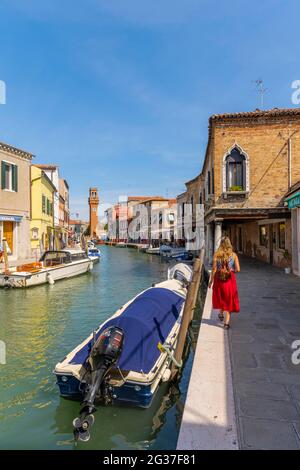 Junge Frau an einem Kanal, Häuser und Boote am Kanal Rio del Vetrai, Glockenturm St. Stefano, Murano, Venedig, Venetien, Italien Stockfoto