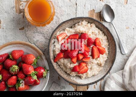 Gekochte Haferflocken-Schüssel mit Erdbeeren auf Betontisch-Hintergrund, Draufsicht. Gesundes Frühstück Stockfoto