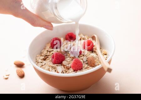 Milch in Hafermüsli gießen. Gesundes Frühstück Müsli Haferflocken Schüssel mit Mandeln und Himbeeren Stockfoto