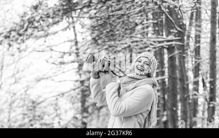 Frau mit Fotokamera. Fotografieren im Winterwald. Fotograf fotografieren am verschneiten Wintertag. Glückliche Frau warme Kleidung Mode. Winter Stockfoto