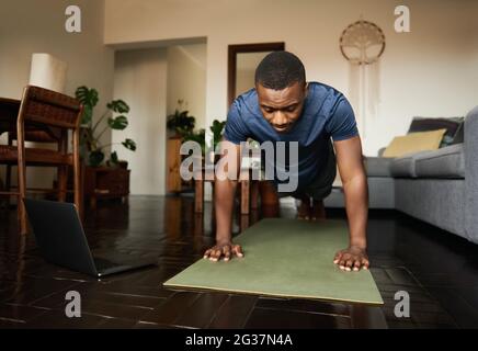 Junger afrikanischer Mann, der zu Hause auf einer Übungsmatte plantscht Stockfoto