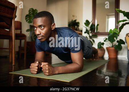 Afrikanischer Mann, der während eines Yoga zu Hause die Unterarmplanke macht Stockfoto