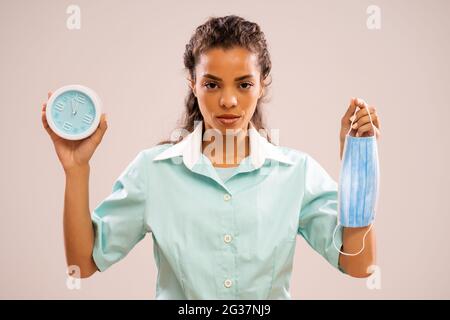 Porträt einer ernsten Krankenschwester, die Schutzkleidung und Uhr hält, die fünf bis zwölf Mal zeigt. Stockfoto
