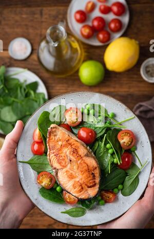 Gesundes Abendessen mit geröstetem Lachssteak und Spinatsalat in männlichen Händen, Draufsicht Stockfoto