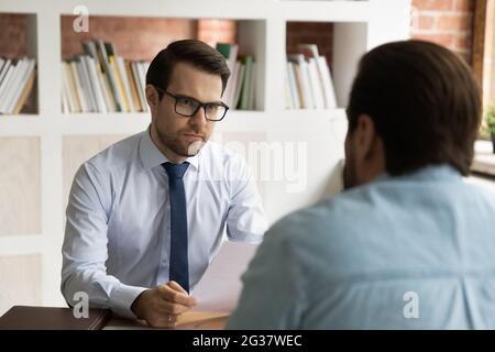 Fokussierter HR-Manager in Brillen, der ein Interview mit dem Bewerber führt. Stockfoto