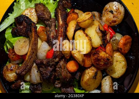 Gegrillte Lammrippen und gebackenes Gemüse auf schwarzem Teller. Draufsicht, flach liegend. Stockfoto