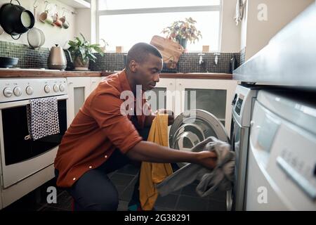 Junger afrikanischer Mann, der zu Hause Kleidung in eine Waschmaschine legt Stockfoto