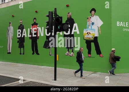 Menschen interagieren mit großen Actionfiguren, die modische Kleidung tragen, gegen einen riesigen grünen Horten, der den Balenciaga-Laden während einer Umrüstung in der vornehmen Gegend auf der Bond Street am 25. Mai 2021 in London, Großbritannien, abdeckt. Diese High-End-Marken sind nebeneinander auf einer sehr gewöhnlichen Wand zu sehen. Die Bond Street ist eine der Hauptstraßen im Einkaufsviertel West End und sehr nobly. Seit dem 18. Jahrhundert ist es eine modische Einkaufsstraße. Die reichen und wohlhabenden Shop hier vor allem für High-End-Mode und Schmuck. Stockfoto