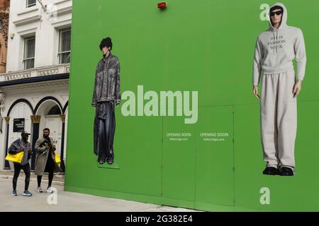 Menschen interagieren mit großen Actionfiguren, die modische Kleidung tragen, gegen einen riesigen grünen Horten, der den Balenciaga-Laden während einer Umrüstung in der vornehmen Gegend auf der Bond Street am 25. Mai 2021 in London, Großbritannien, abdeckt. Diese High-End-Marken sind nebeneinander auf einer sehr gewöhnlichen Wand zu sehen. Die Bond Street ist eine der Hauptstraßen im Einkaufsviertel West End und sehr nobly. Seit dem 18. Jahrhundert ist es eine modische Einkaufsstraße. Die reichen und wohlhabenden Shop hier vor allem für High-End-Mode und Schmuck. Stockfoto