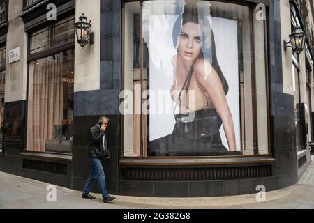 Großformatige Werbebilder der Luxusmarke Burberry in Schaufenstern entlang der Regent Street am 26. Mai 2021 in London, Großbritannien. Vorbeifahrende Menschen interagieren mit den riesigen Figuren auf diesen Fotos, als ob sie im Vergleich winzig wären. Dieses Gebiet der Hauptstadt ist bekannt für seine exklusiven Geschäfte, deren Geschäfte sich an die Reichen und Reichen richten. Stockfoto