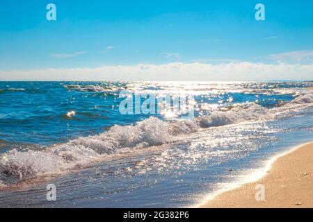 Ein blaues glitzerndes Meer mit einer Welle, die auf dem Sand rollt. Ruhen Sie sich an der Küste aus. Stockfoto