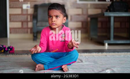 Kinder Yoga. Kleiner indischer Junge, der Yoga-Übungen macht und Anweisungen im Fernsehen sieht. Stockfoto