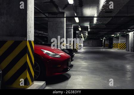 Dunkler landschaftlich schöner Parkplatz in einer mehrstufigen Tiefgarage. Betonzementsäule überdachtes Gebäude Untergeschoss Parkplatz für Elektrofahrzeuge Stockfoto