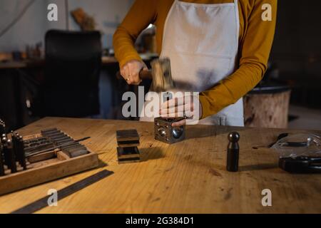 Mittelteil der kaukasischen Juwelierin mit Schürze, mit Hammer, Schmuck zu machen Stockfoto