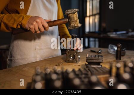 Mittelteil der kaukasischen Juwelierin mit Schürze, mit Hammer, Schmuck zu machen Stockfoto