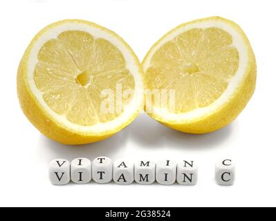 Frisch geschnittene reife Zitrone mit VITAMIN C-Wort aus Mini-Buchstabenwürfeln auf weißem Hintergrund isoliert Stockfoto