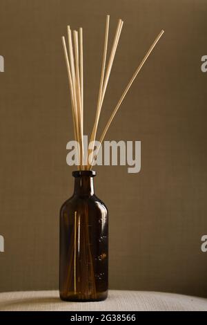 Diffusor-Flasche aus dunklem Glas mit natürlichen Schilfrohrstäben auf einem Kissen Stockfoto