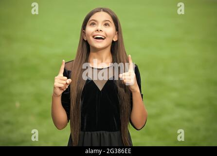 Inspiriert glücklich Mädchen mit langen Haaren in Mode Kleid Look up halten indeex Finger angehoben grünen Gras Sommer im Freien, Inspiration Stockfoto