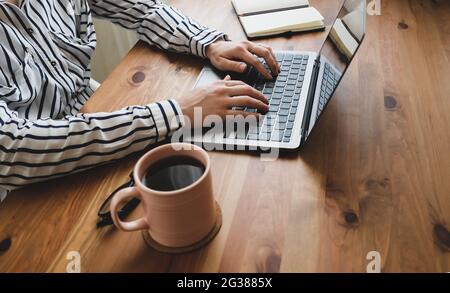 Junge Frau, die am Tisch mit Kaffee, Laptop und Notizblock arbeitet. Stockfoto