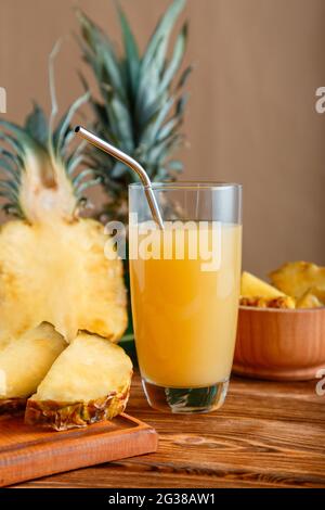 Ananassaft im Glas. Glas frischer natürlicher Ananassaft Cocktail mit wiederverwendbarem Metallrohr auf braunem Holztisch mit Zutaten. Roh Stockfoto