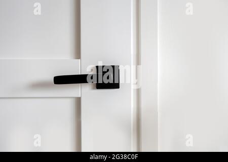Moderne und stilvolle weiße Holztür mit schwarzem Türgriff Innenarchitektur, Nahaufnahme Hintergrundtextur Innendekoration eines modernen Hauses Stockfoto