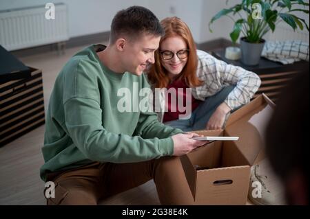 Neue Hausbesitzer haben an ihrer Wohnung angehalten, sie sortieren Kartons, ein Mann zeigt einer Frau sein altes Foto. Stockfoto