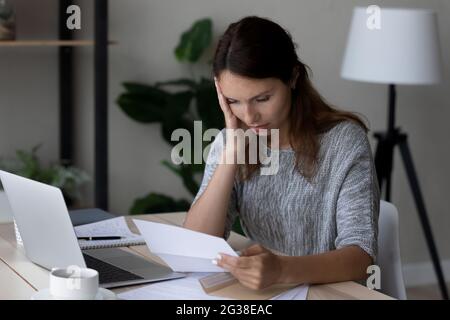 Unglückliche frustrierte Frau, die unerwartete schlechte Nachrichten in einem Brief liest Stockfoto