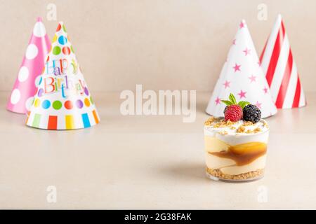 Süße Desserts mit frischen Beeren und Geburtstagshut auf hellem Hintergrund. Stockfoto