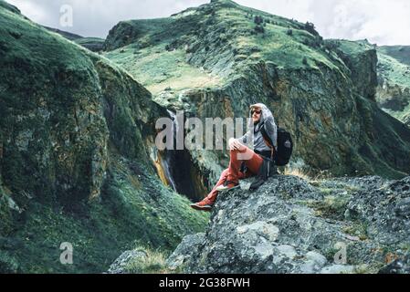 Der Reisende sitzt auf einem Stein in den Bergen Stockfoto