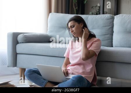 Unglückliche müde arabische Frau, die den Hals berührt und am Laptop arbeitet Stockfoto
