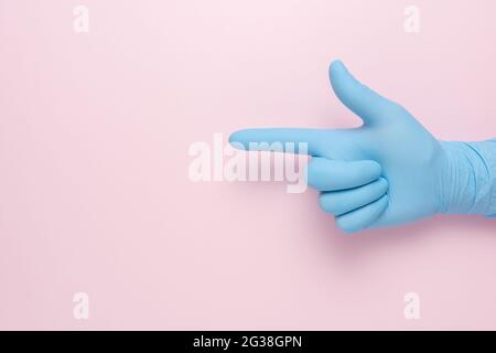 Hand im blauen Handschuh zeigt die Geste einer Pistole auf rosa Hintergrund. Minimales flaches Lay-Konzept. Stockfoto