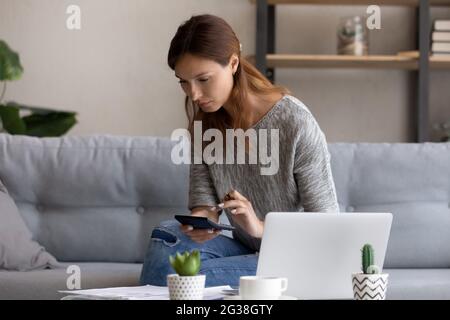 Fokussierte Frau, die Ausgaben oder Inlandsrechnungen berechnet, mit dem Rechner Stockfoto