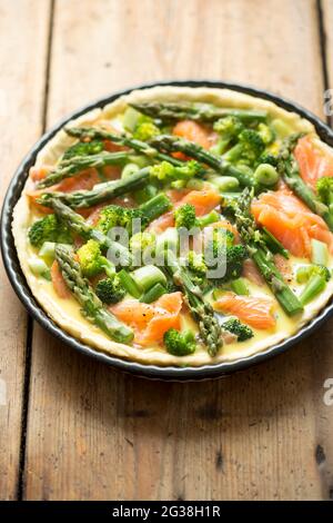Zubereitung von Quiche mit Lachs, Brokkoli und grünem Spargel, überzogen mit Milch- und Eiermischung. Rohe Tarte - Ofen fertig. Stockfoto