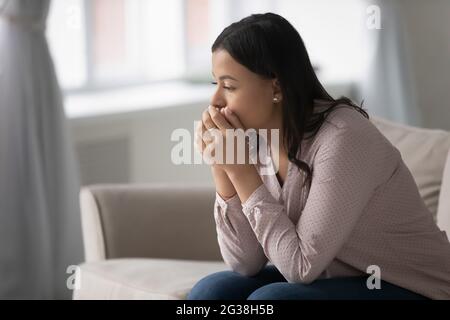 Nachdenkliche, besorgt gemischte Rasse Frau, die zu Hause auf der Couch sitzt Stockfoto