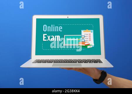 Männliche Hand hält Laptop mit Text ONLINE-TEST vor farbigem Hintergrund Stockfoto