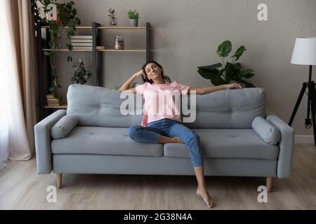 In voller Länge lächelnde arabische Frau, die sich zu Hause auf der Couch entspannt Stockfoto