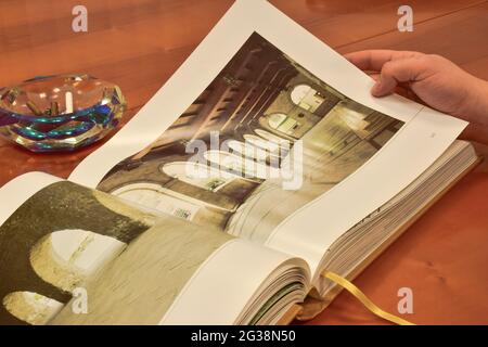 Ein offenes großes Buch liegt auf einem braunen Holztisch, dahinter ein Aschenbecher mit mehreren gerauchten Zigarren Stockfoto
