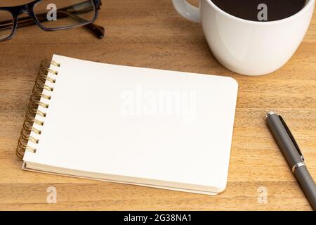 Spiralnotepad-Mockup-Schablone mit Kaffeetasse und Brillen auf Holztisch. Leeres White Paper Stockfoto