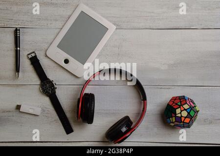 Auf einem beigen Holztisch liegen ein E-Book, eine Armbanduhr, ein Rubik-Würfel, Kopfhörer und ein Stift. Rechts neben dem Foto befindet sich ein leerer Bereich Stockfoto