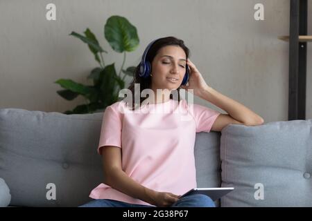 Lächelnde arabische Frau in Kopfhörern, die Tablet hält und Musik genießt Stockfoto