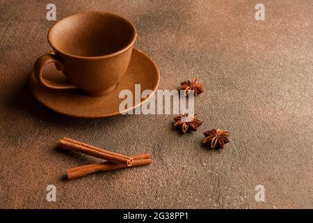 Leere braune Tasse aus Keramik mit Untertasse, Zimt und Anisgestein auf Steinoberfläche Stockfoto